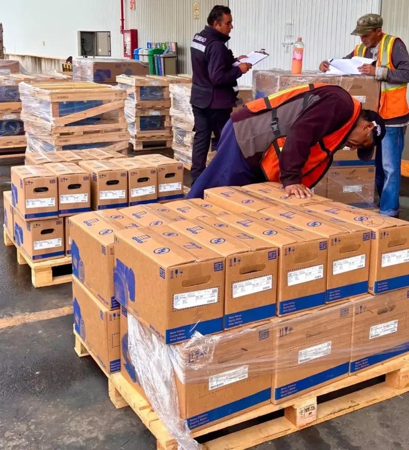 Trabajadores revisando cajas de bombas de agua en un área de almacenamiento, con palets apilados de forma ordenada.